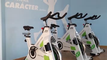 Trois vélos d’appartement dans une pièce dont un mur est bleu et sur lequel figure un texte motivant.