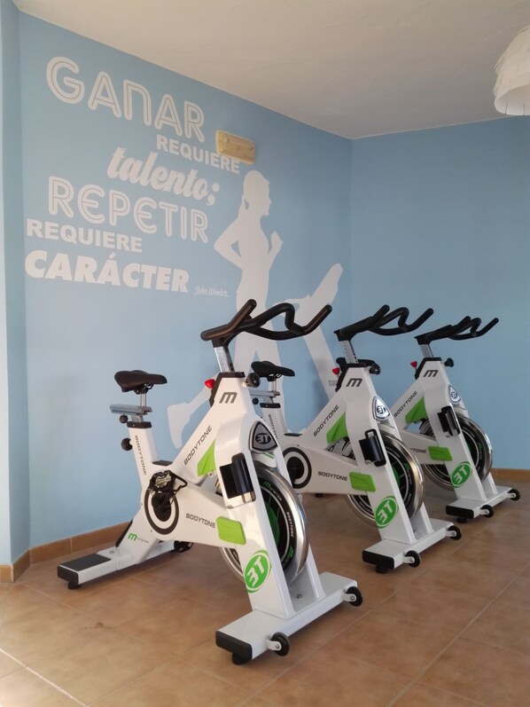Three stationary bikes in a room with a blue wall and motivational text. - Apartamentos Hesperia Bristol Playa (La Oliva)