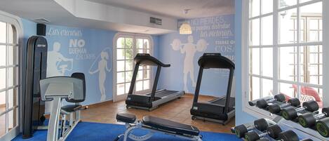 Une salle de sport équipée de tapis de course, d’un banc de développé couché et d’haltères.