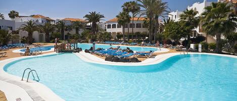A large swimming pool with blue lounge chairs and palm trees.