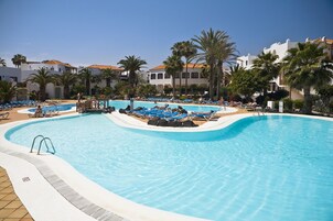 Una piscina amplia con sillones reclinables azules y palmeras.