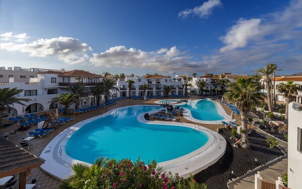 A resort with multiple swimming pools, sun loungers, and palm trees.