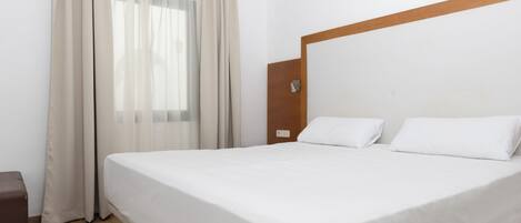Ein Hotelzimmer mit einem großen Bett, einem Holz-Kopfteil, einem kleinen Nachttisch und einem Fenster mit Vorhängen.