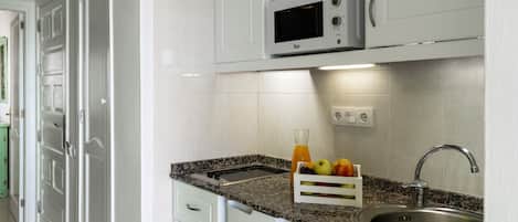 A kitchen with white cabinets, a microwave, a sink, and a fruit basket.