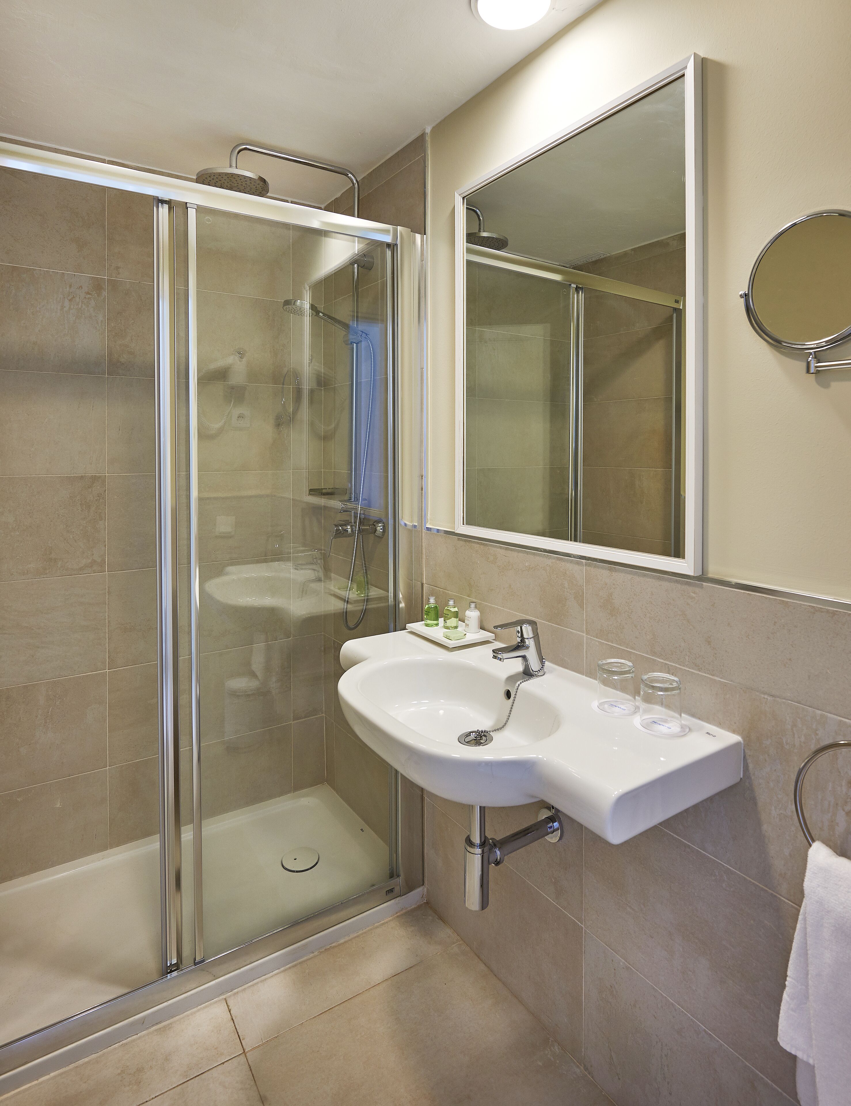 A modern bathroom with a glass-enclosed shower, a white sink with a mirror above it, and beige tiles.