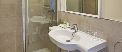 A modern bathroom with a glass-enclosed shower, a white sink with a mirror above it, and beige tiles.