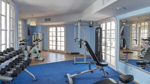 A gym with exercise equipment, a blue carpet, and large windows. - Apartamentos Hesperia Bristol Playa (La Oliva)