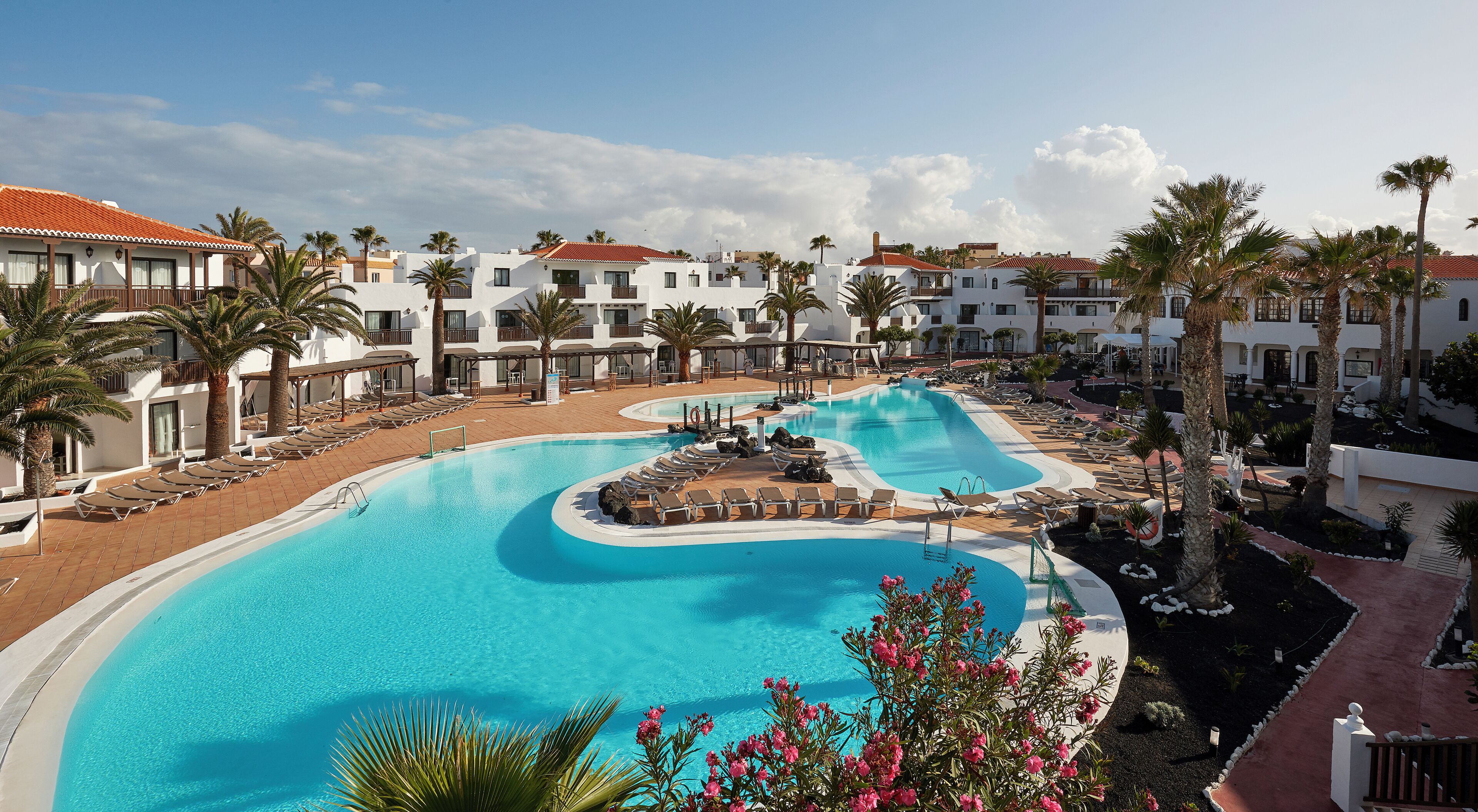 Ein Resort mit einem großen Schwimmbad, Liegestühlen und Palmen.