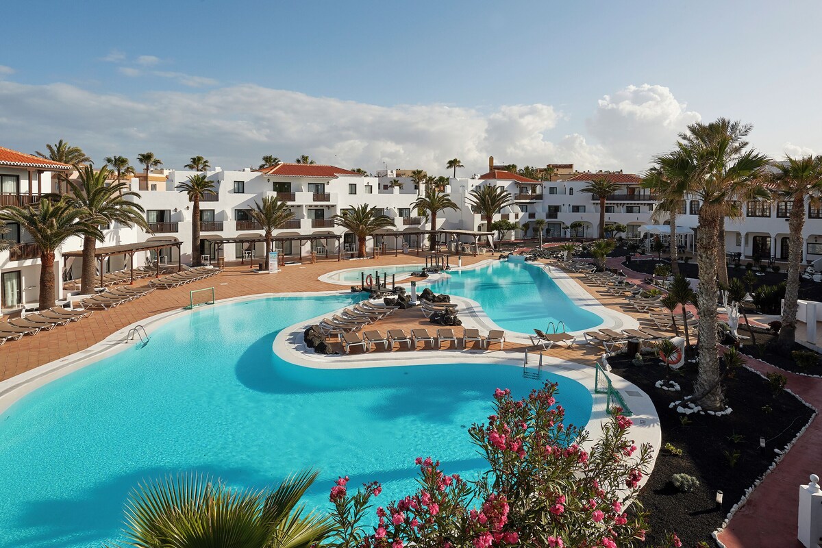 Un resort con una amplia piscina, tumbonas y palmeras.