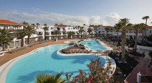 A resort with a large swimming pool, sun loungers, and palm trees.