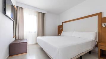A hotel room with a large bed, a TV mounted on the wall, a wooden headboard, and a small wooden nightstand.