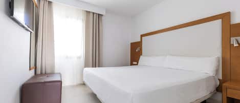 A hotel room with a large bed, a TV mounted on the wall, a wooden headboard, and a small wooden nightstand.