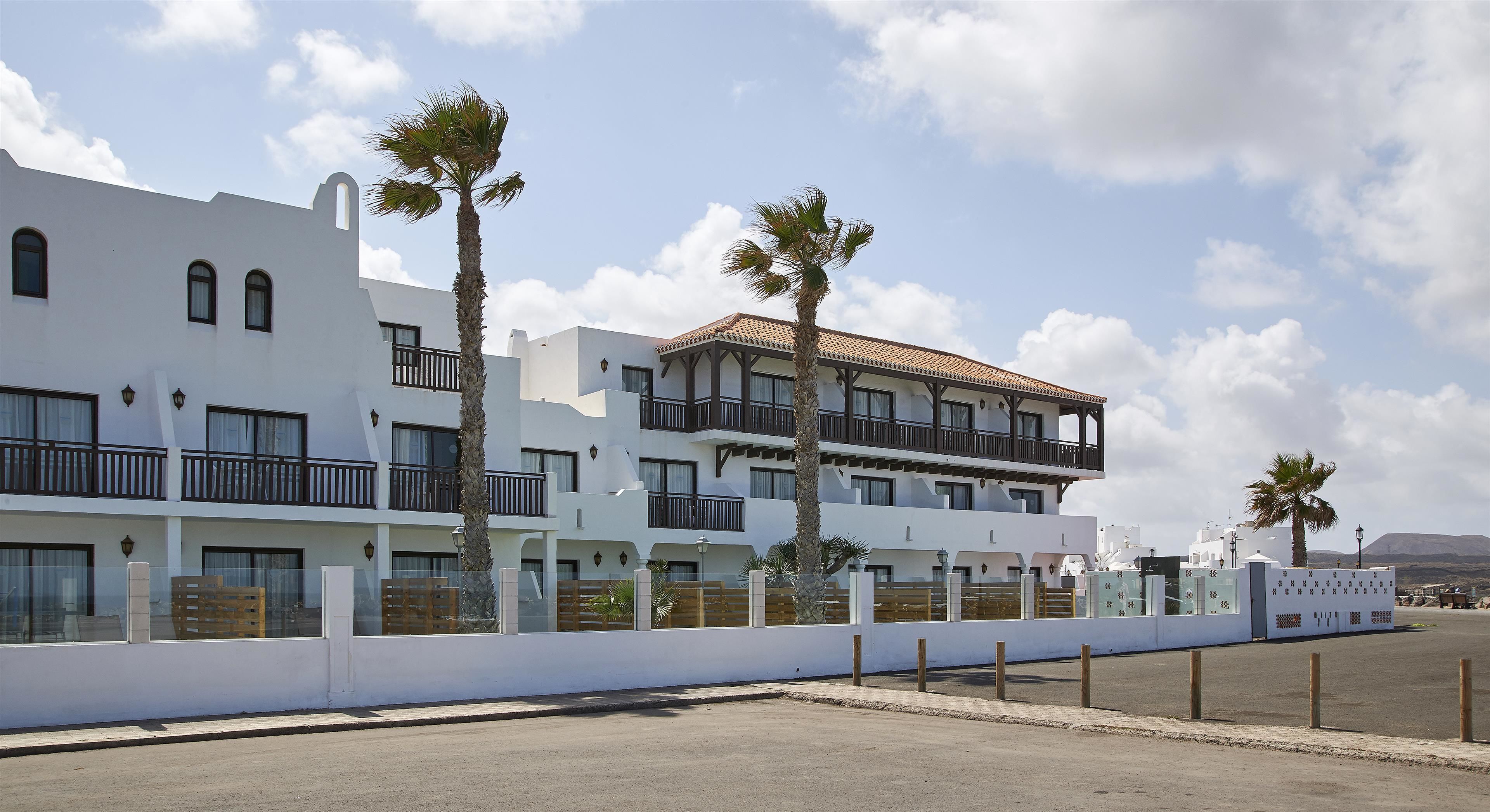A modern hotel with multiple balconies, palm trees, and a clear sky.