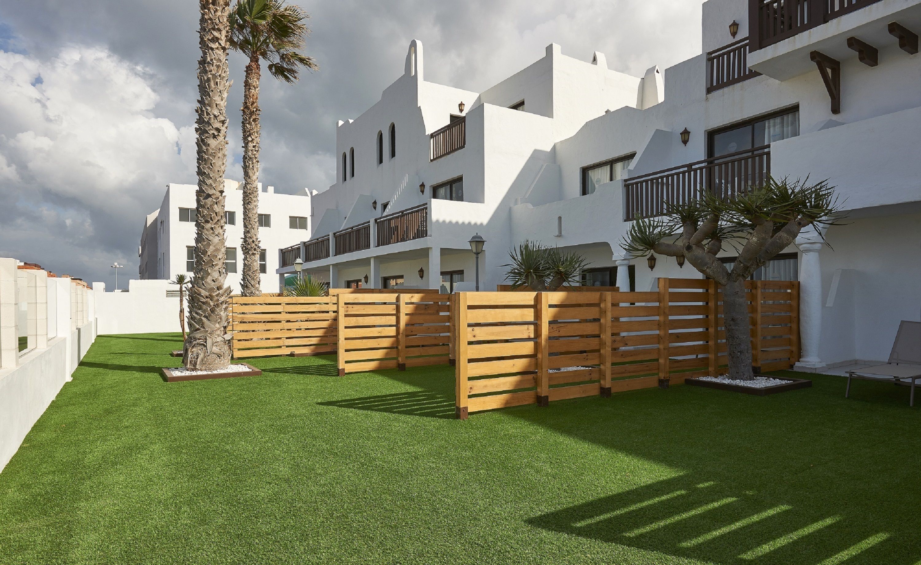Un edificio moderno con paredes exteriores blancas, varios balcones y un césped bien cuidado de césped artificial.