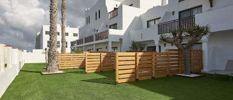 A modern building with white exterior walls, multiple balconies, and a well-maintained lawn with artificial grass.