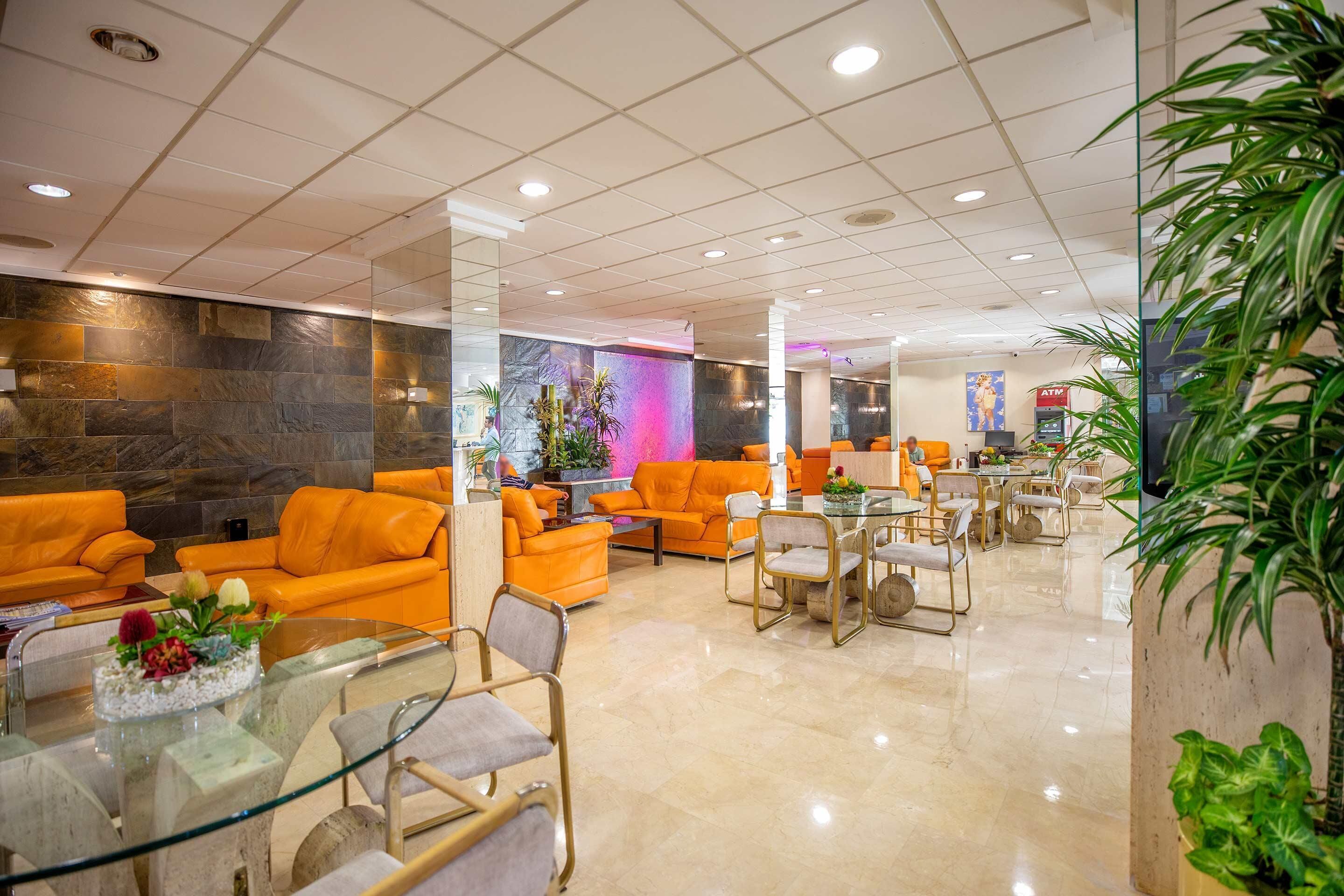 Un vestíbulo moderno con sofás naranja, una mesa de centro de vidrio y una pared de piedra.