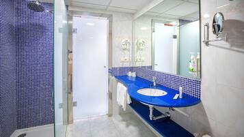 Un baño con ducha revestida en azul, un lavamanos blanco con encimera azul, y un espejo con una toalla colgada en la pared.
