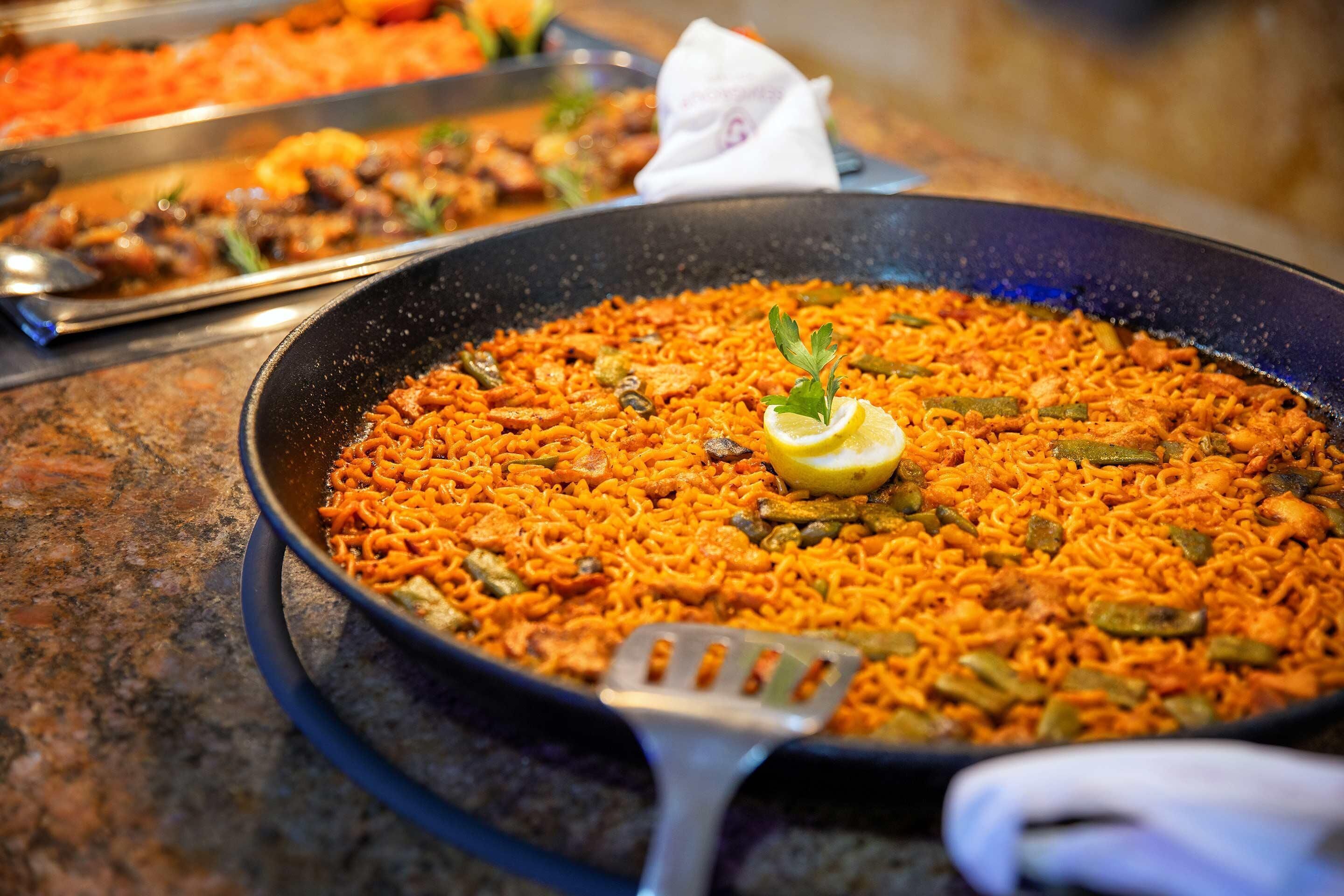 A large pan of paella with vegetables and a lemon garnish.