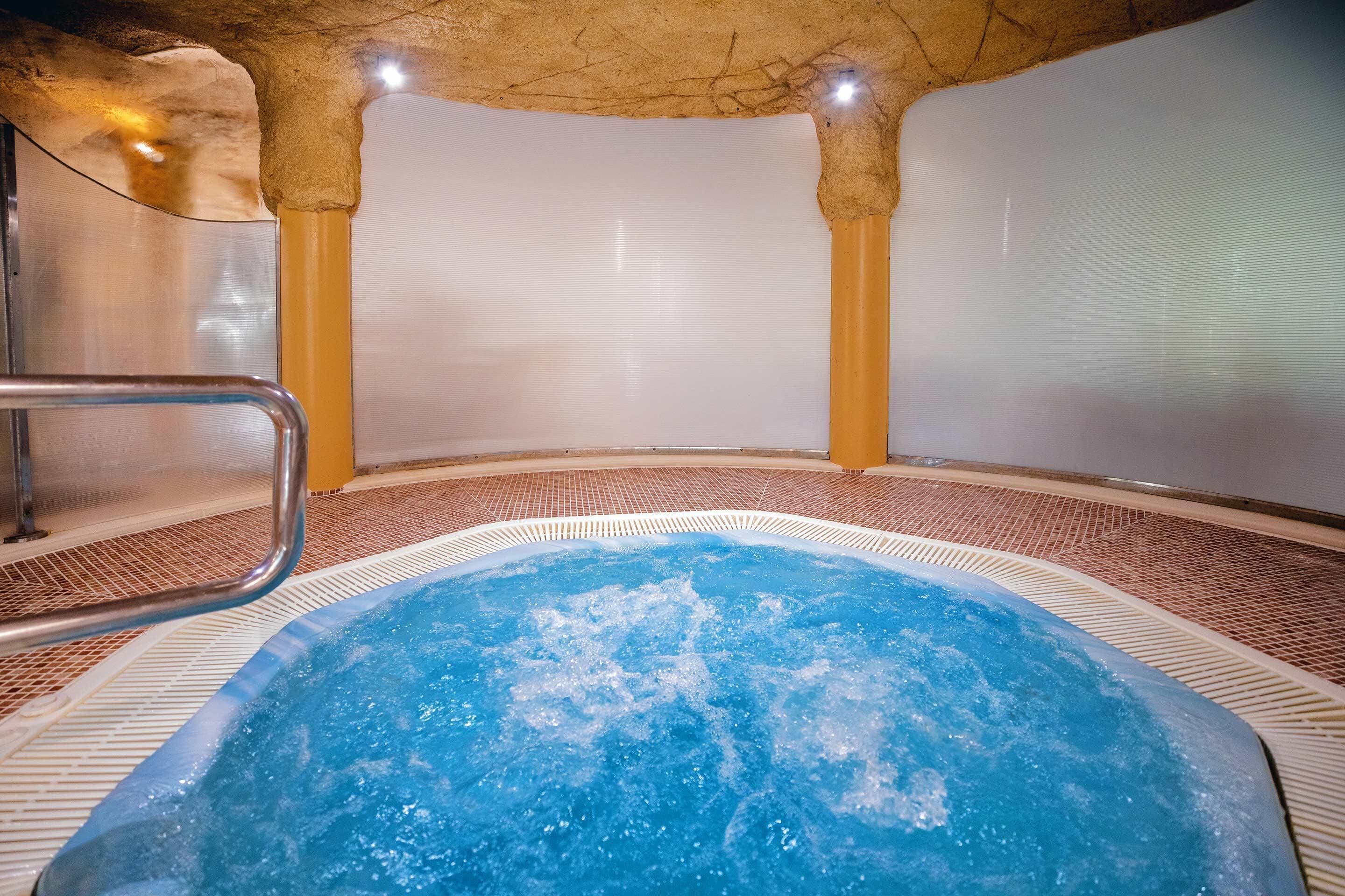 Un bain à remous doté d’un sol carrelé et d’une rambarde en métal.