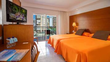 Habitación de hotel con dos camas, televisión, escritorio con silla y balcón con vistas a edificios.