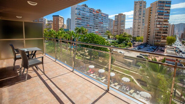 Un balcon avec une table et des chaises, donnant sur un paysage urbain avec de hauts immeubles et des palmiers.