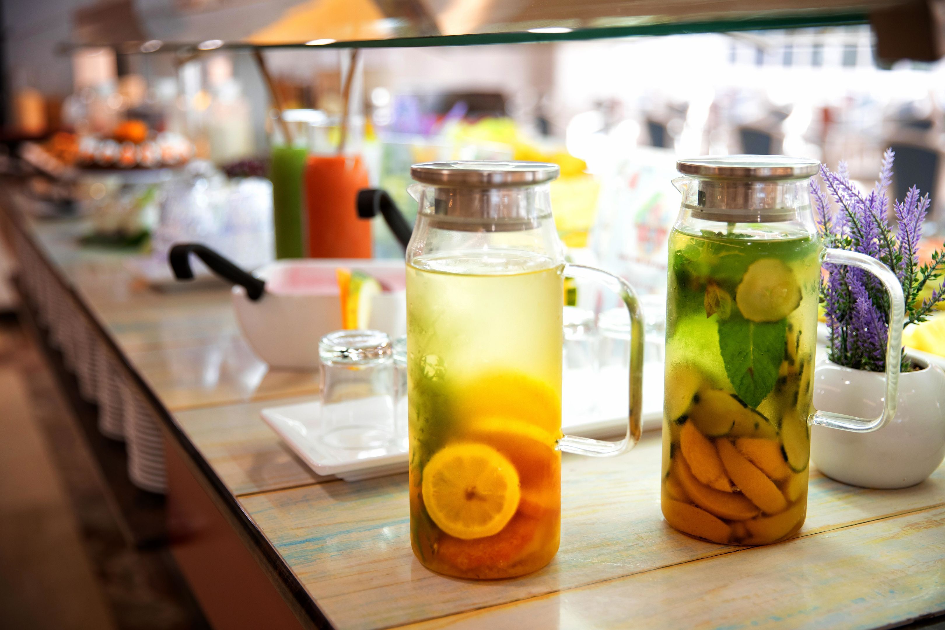 Dos recipientes de vidrio con frutas y hierbas, probablemente para preparar bebidas infusionadas, sobre una mesa con una separación de vidrio.