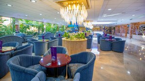 Un hall d’hôtel moderne avec des sièges bleus, une table ronde centrale et un lustre décoratif.