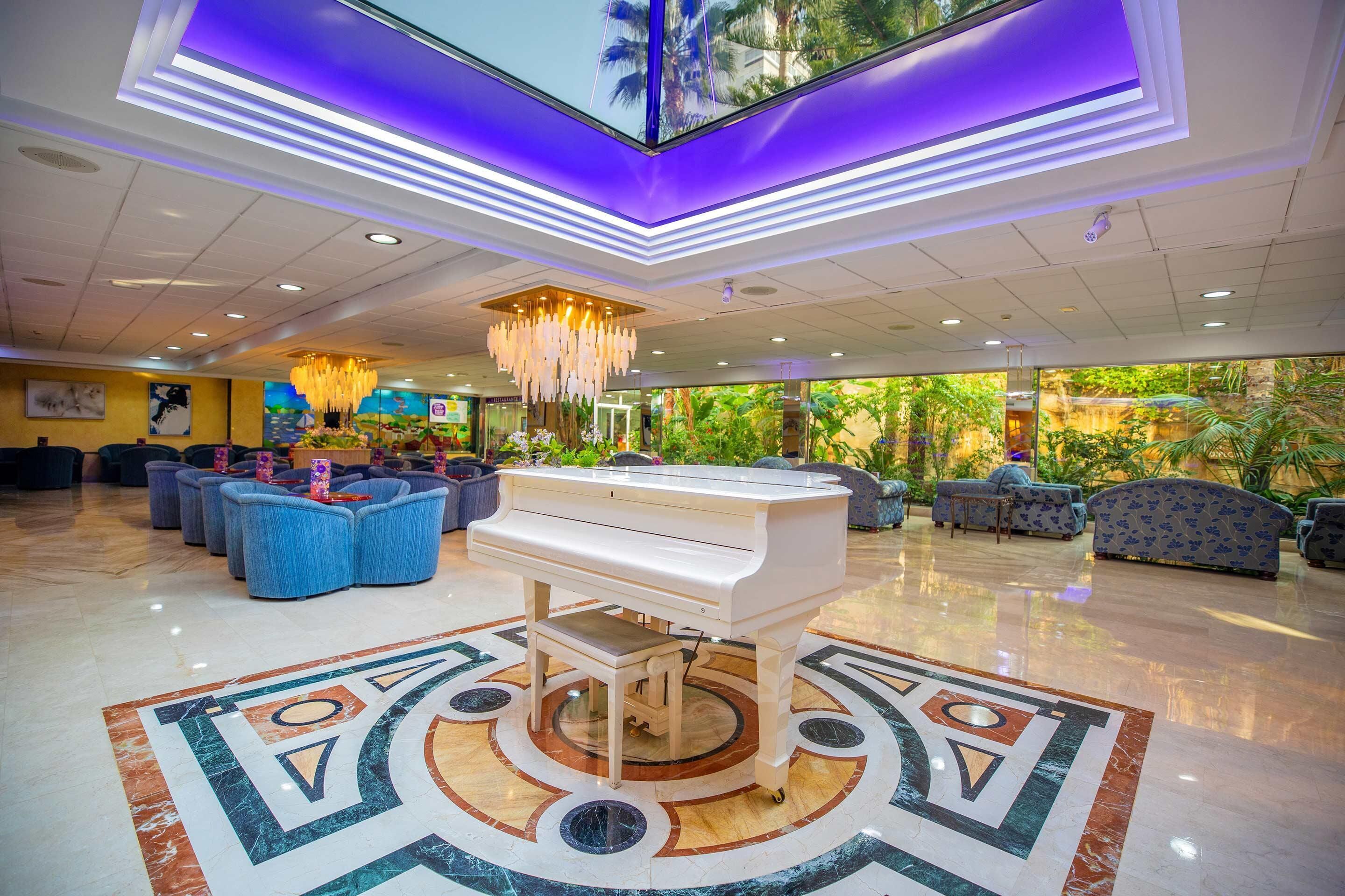 Een lobby met een vleugelpiano, luxe zitplaatsen, een kroonluchter en een groot raam met uitzicht op groen.