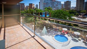 Un balcon doté d’une rambarde en verre, donnant sur un espace piscine aménagé avec des chaises longues et des parasols.