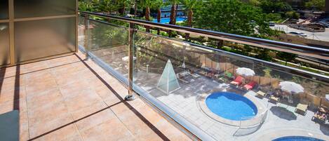 A balcony with a glass railing overlooking a pool area with lounge chairs and umbrellas.