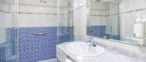 Un baño con ducha envuelta en vidrio, un lavabo blanco y un salpicadero de azulejos.