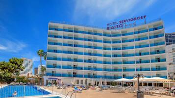 Un hotel con zona de piscina, varios balcones y un cielo azul despejado.