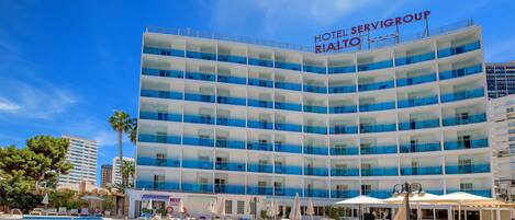 Un hotel con zona de piscina, varios balcones y un cielo azul despejado.