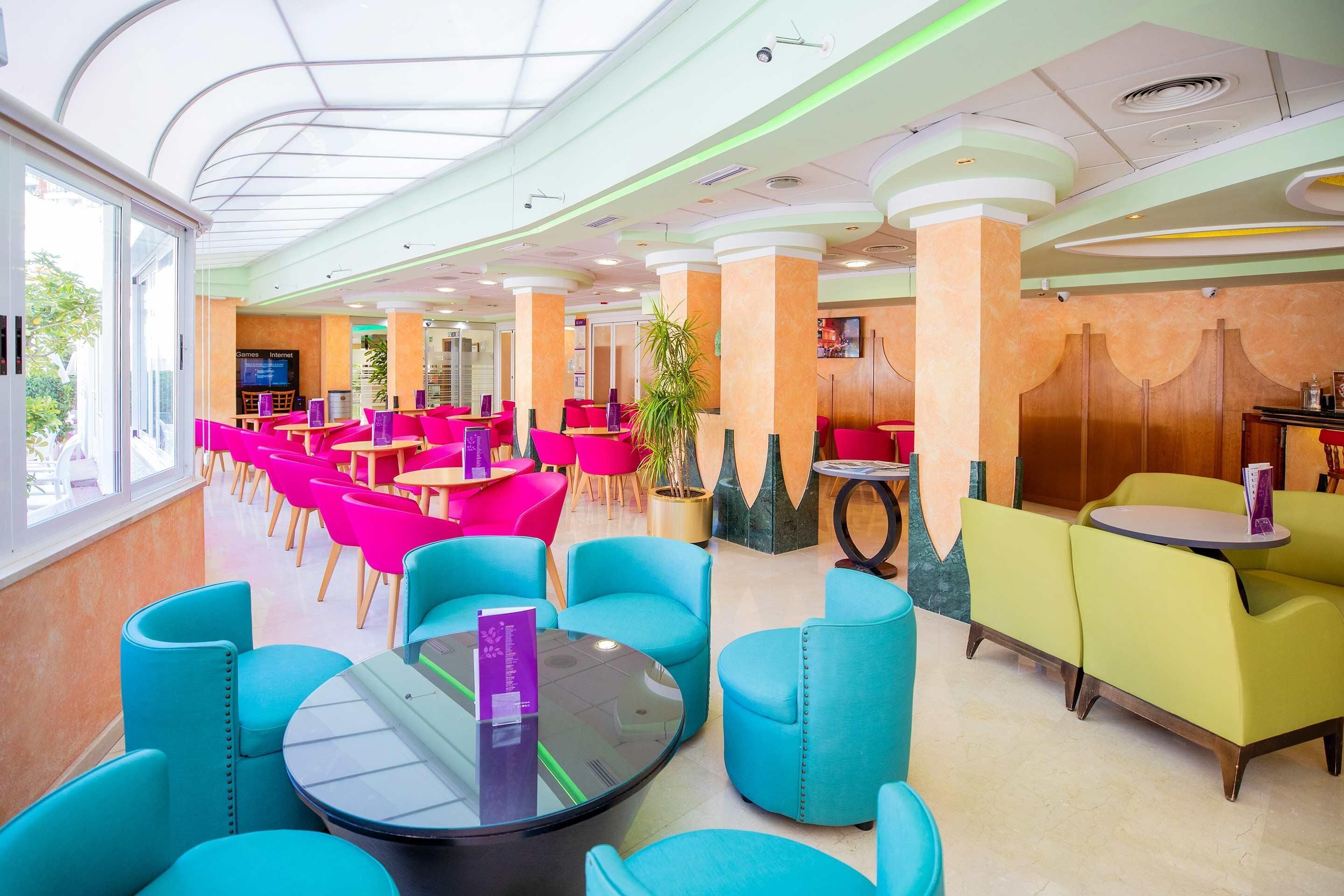 A modern indoor seating area with round tables and chairs, a large window, and a television screen.