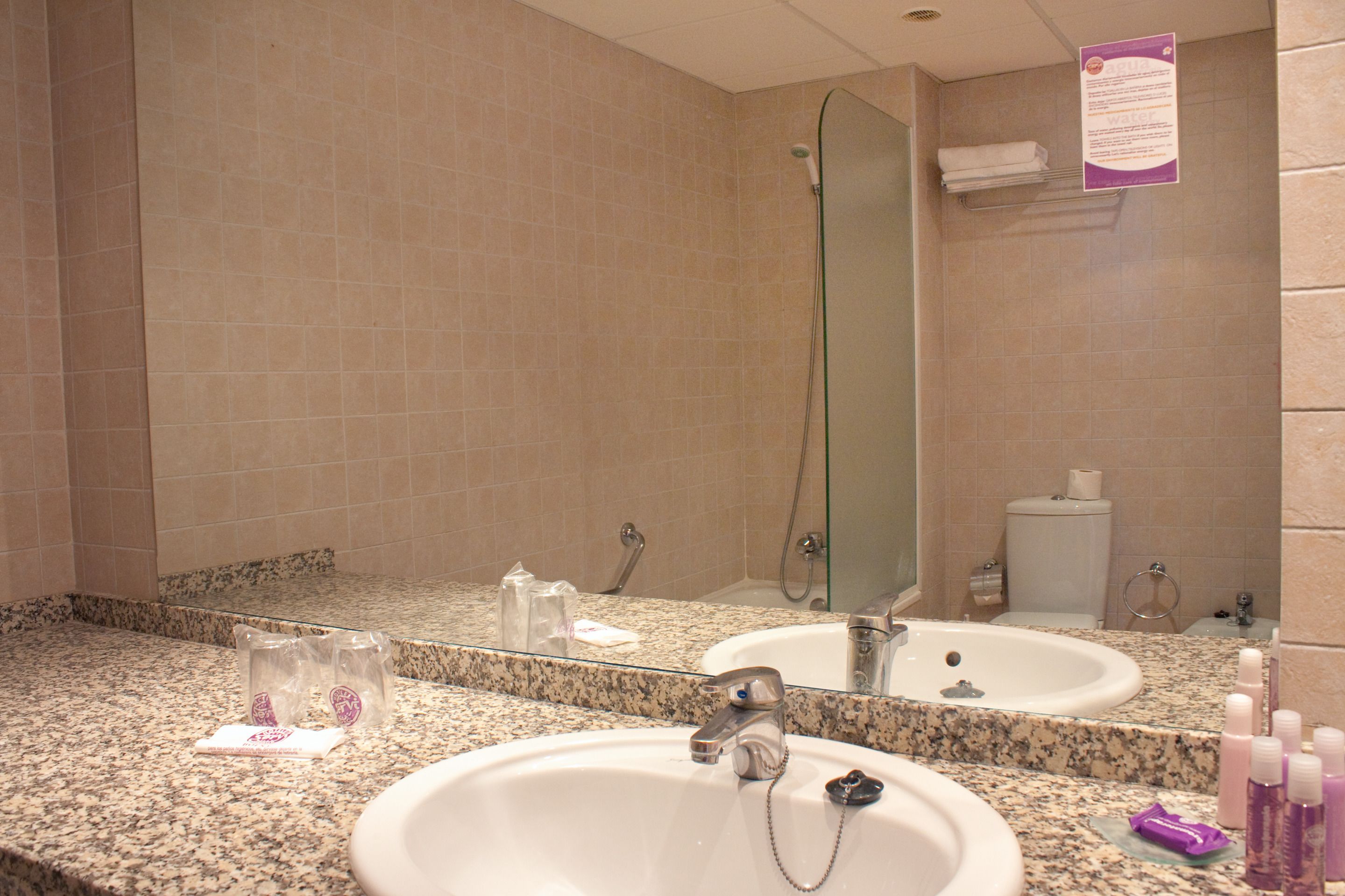Un baño con encimera de granito, un lavabo blanco, un espejo y artículos de aseo en la encimera.