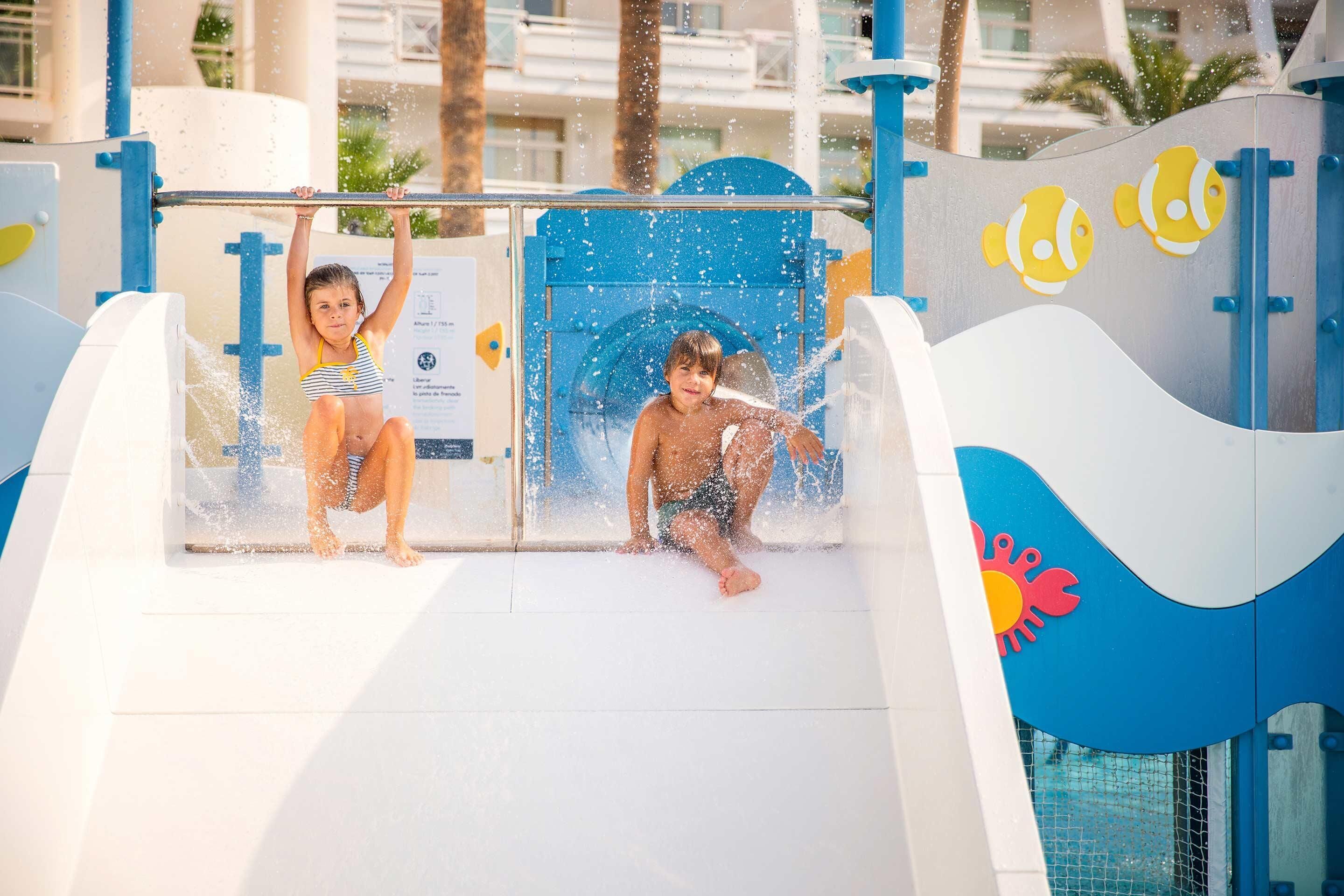 A water play area with slides and splash zones, featuring cartoon fish and crab decorations.
