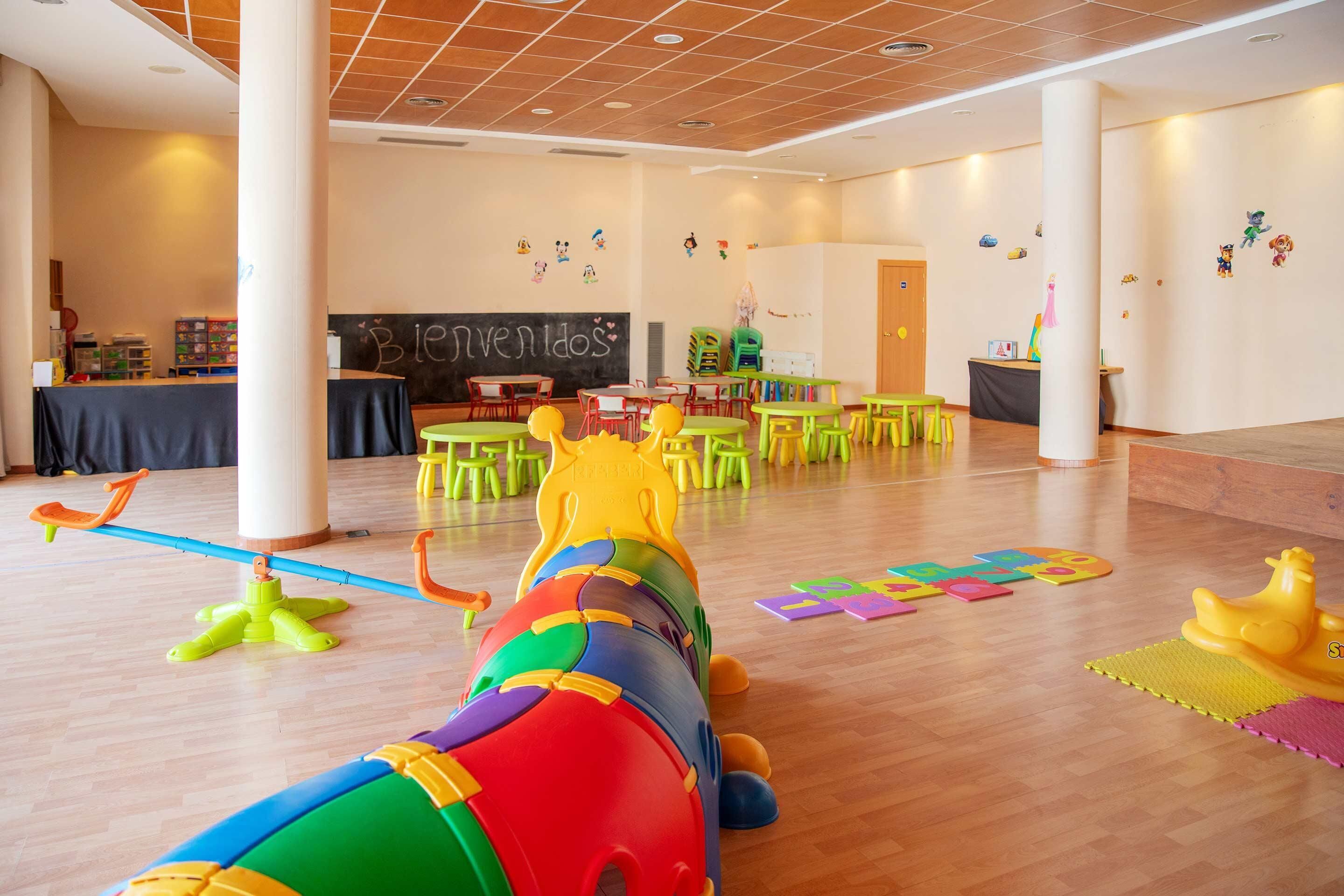 Un grand espace de jeux intérieur, doté d’équipements colorés, de tables et de chaises.
