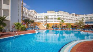 A hotel pool area with a clear blue pool, lounge chairs, and a staircase leading to the upper floors.