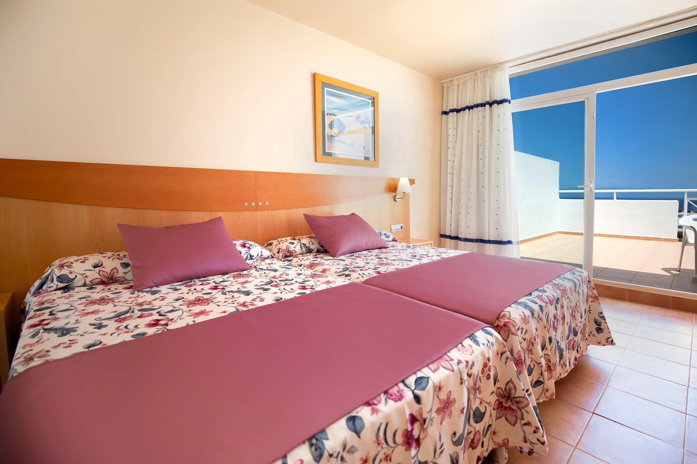 A hotel room with a large bed, a wooden headboard, a window with curtains, and a view of the sky.