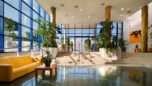 En rummelig lobby med en gul sofa, et sofabord og potteplanter.