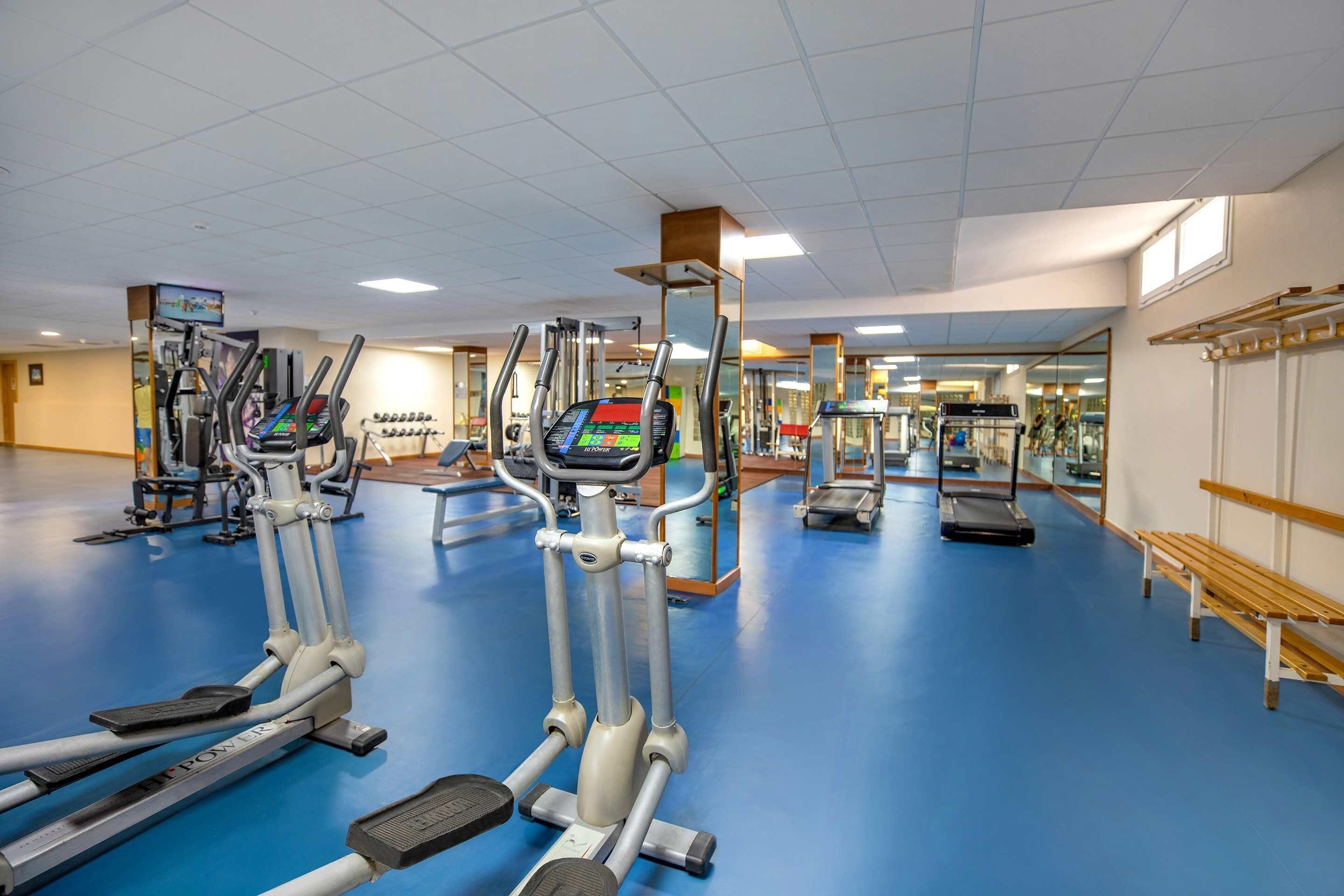 Een sportschool met loopbanden, crosstrainers en een bank.