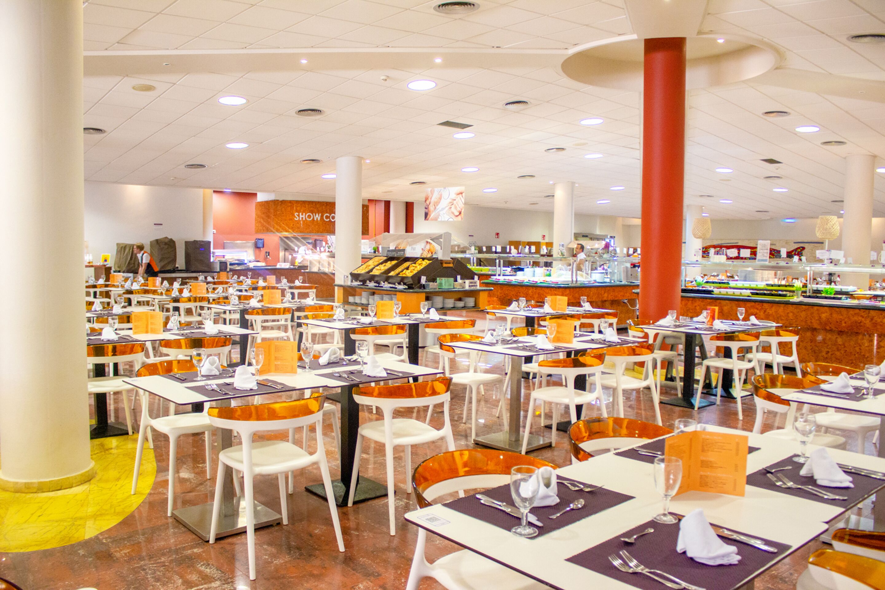 Un restaurante amplio con varias mesas y sillas, una barra central con mostrador y un interior luminoso y bien iluminado.