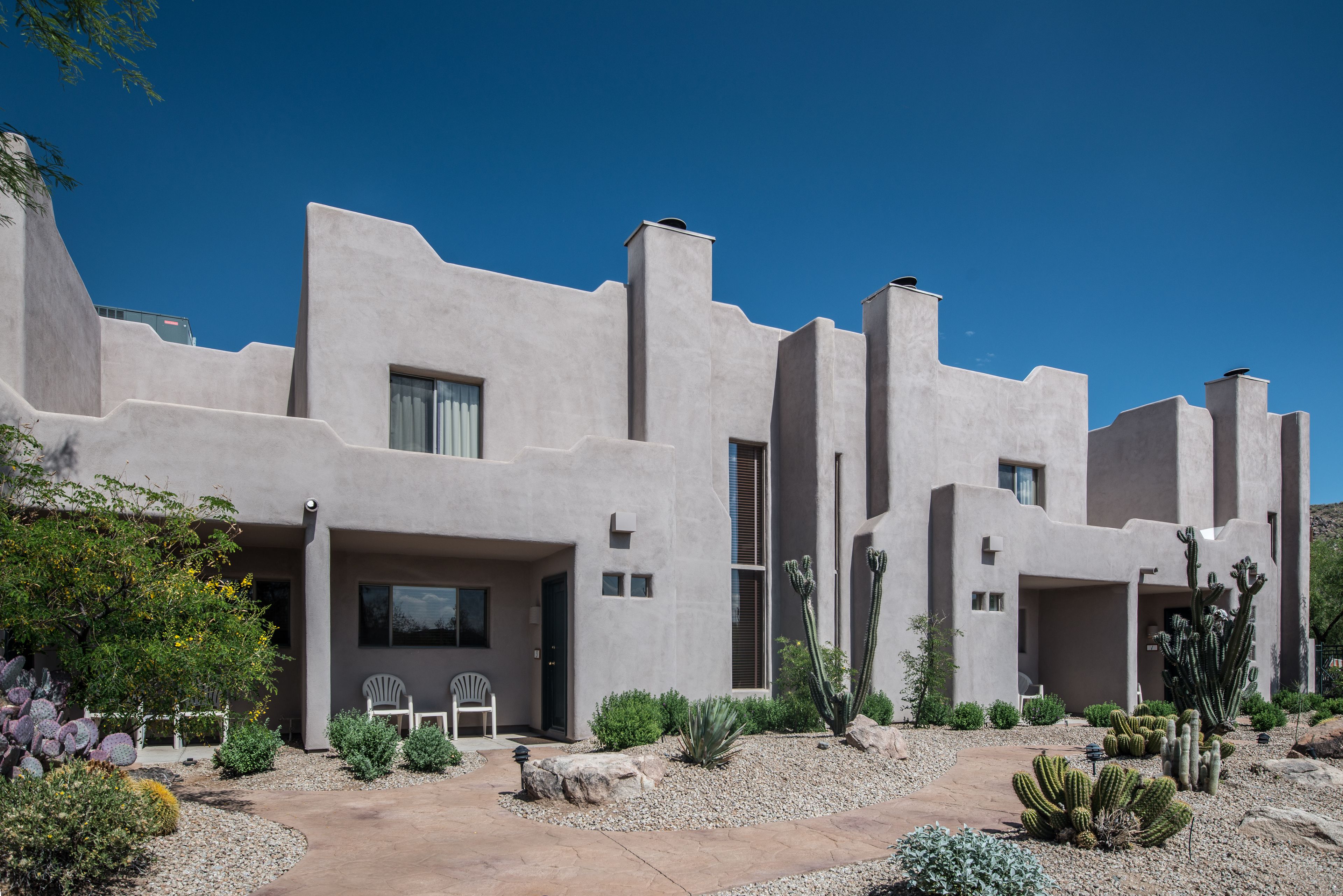 Une maison moderne dotée d’un style architectural unique, avec plusieurs entrées et un jardin bien entretenu où l’on peut admirer différentes espèces de cactus.