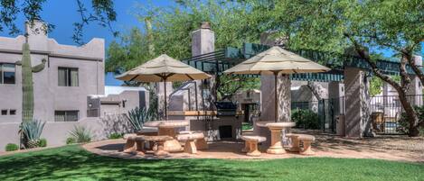 Un patio con mesas y sillas de piedra, rodeado de césped cuidado y cactus.