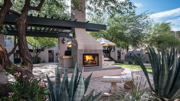 An outdoor patio with a stone fireplace, surrounded by cacti and trees. - Villas of Cave Creek (Cave Creek)