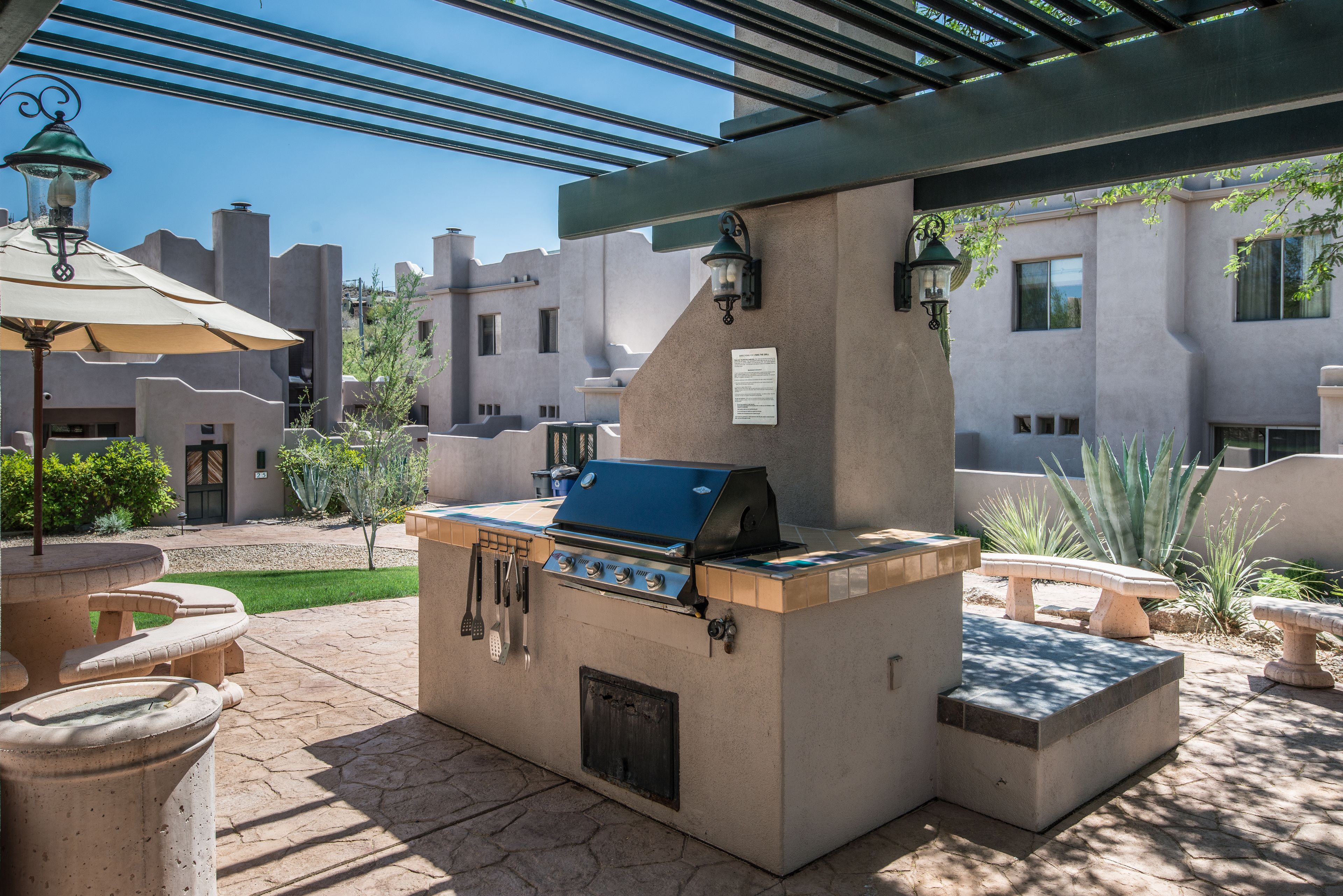 An outdoor barbecue area with a grill, stone tables, and a pergola.