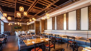 A modern restaurant interior with wooden tables, cushioned seating, and hanging pendant lights. - Hilton Miami Dadeland (Miami)
