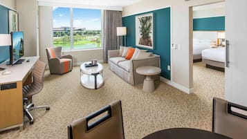 A hotel room with a desk, office chair, sofa, and bed. There is a window with a view of a golf course.