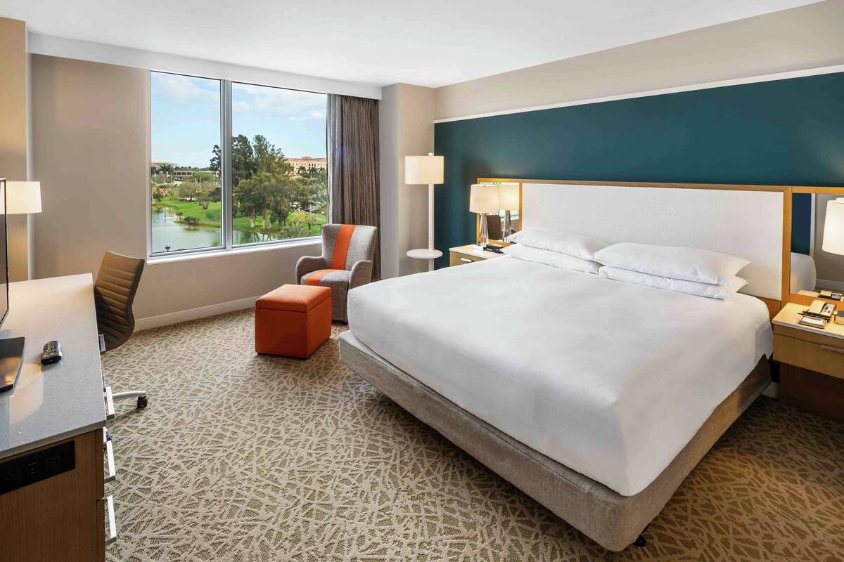 A hotel room with a large bed, a desk, a chair, and a view of a lake.