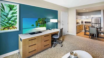 Quarto de hotel moderno com televisão, mesa de trabalho e cozinha compacta.
